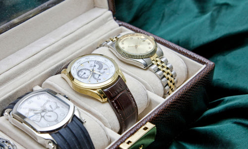 Luxury watches displayed in a watch case featuring leather straps and metal bracelet bands, showcasing classic and premium timepiece styles.
