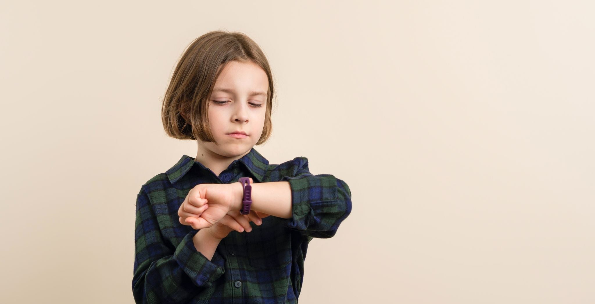 Young child checking the time on a wristwatch, wearing a casual shirt, illustrating a kid learning to tell time with a child-friendly watch.