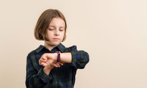 Young child checking the time on a wristwatch, wearing a casual shirt, illustrating a kid learning to tell time with a child-friendly watch.